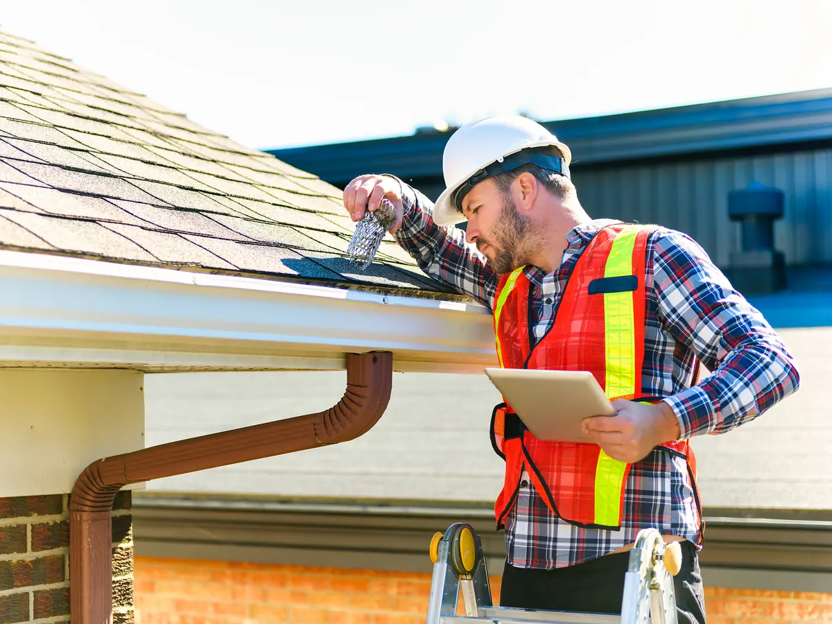 Roof inspector with a tablet checking shingles at the gutter